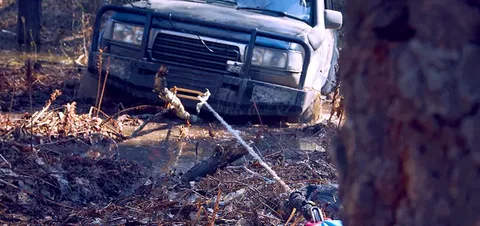 A 4x4 truck stuck deep in mud being pulled out by a steel cable hook, illustrating the difference between a Winch Out vs. Towing service