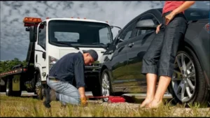 A professional technician changing a tire next to a tow truck, offering emergency Roadside Assistance to a stranded driver