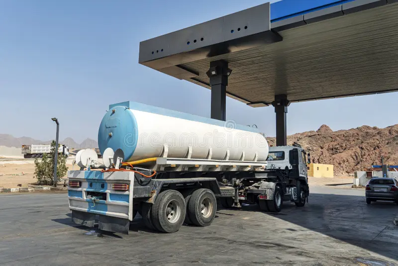 A large commercial tanker truck parked at a gas station station for Fuel Delivery services